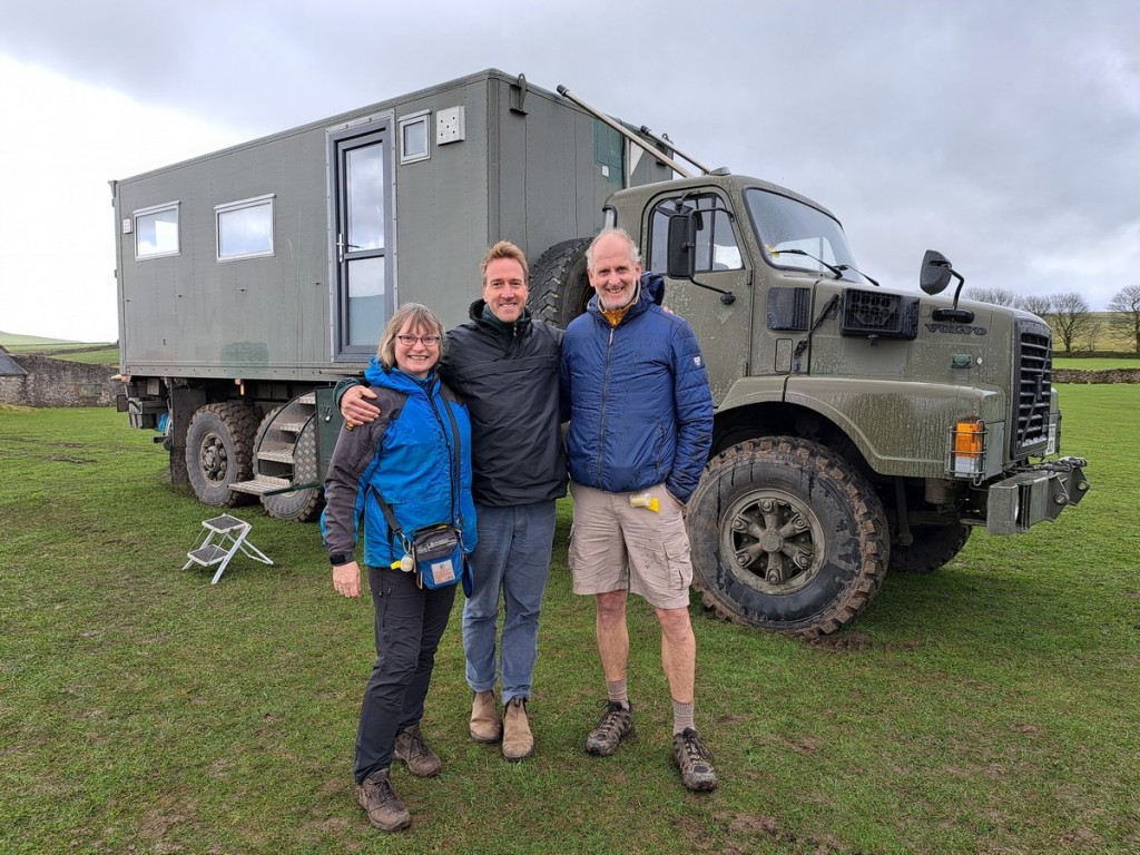 A photo of The Beast, a NATO green Volvo N10 bull nosed truck, with New Lives in the Wild TV presenter Ben Fogle flanked by author Jacqueline Lambert and her husband Mark. 