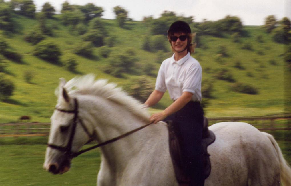 A picture of author Jacqueline Lambert on her horse, Colonel, a white 3/4 thoroughbred, cantering with the background blurred to show how fast he's travelling. The photo is to illustrate that life is too short for anything other than a wild ride
