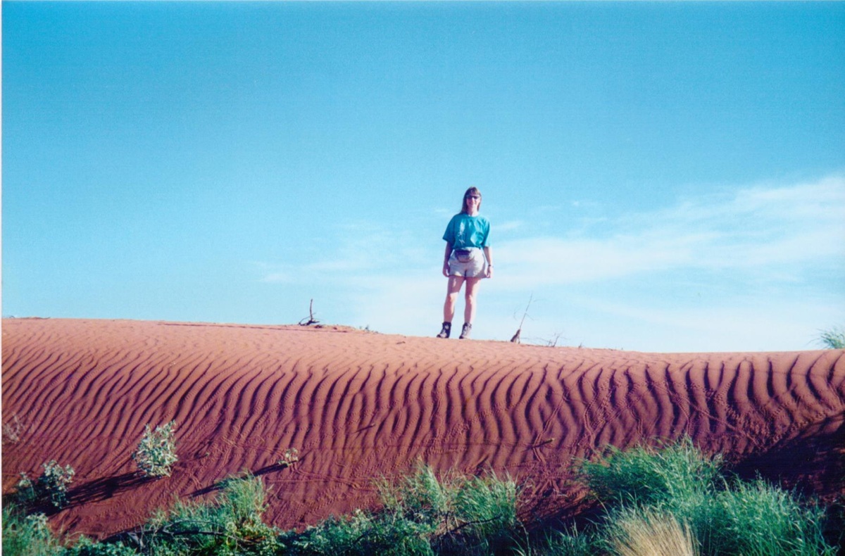 Author Jacqueline Lambert standing on a rippled deep red sand dune in the red centre of Australia