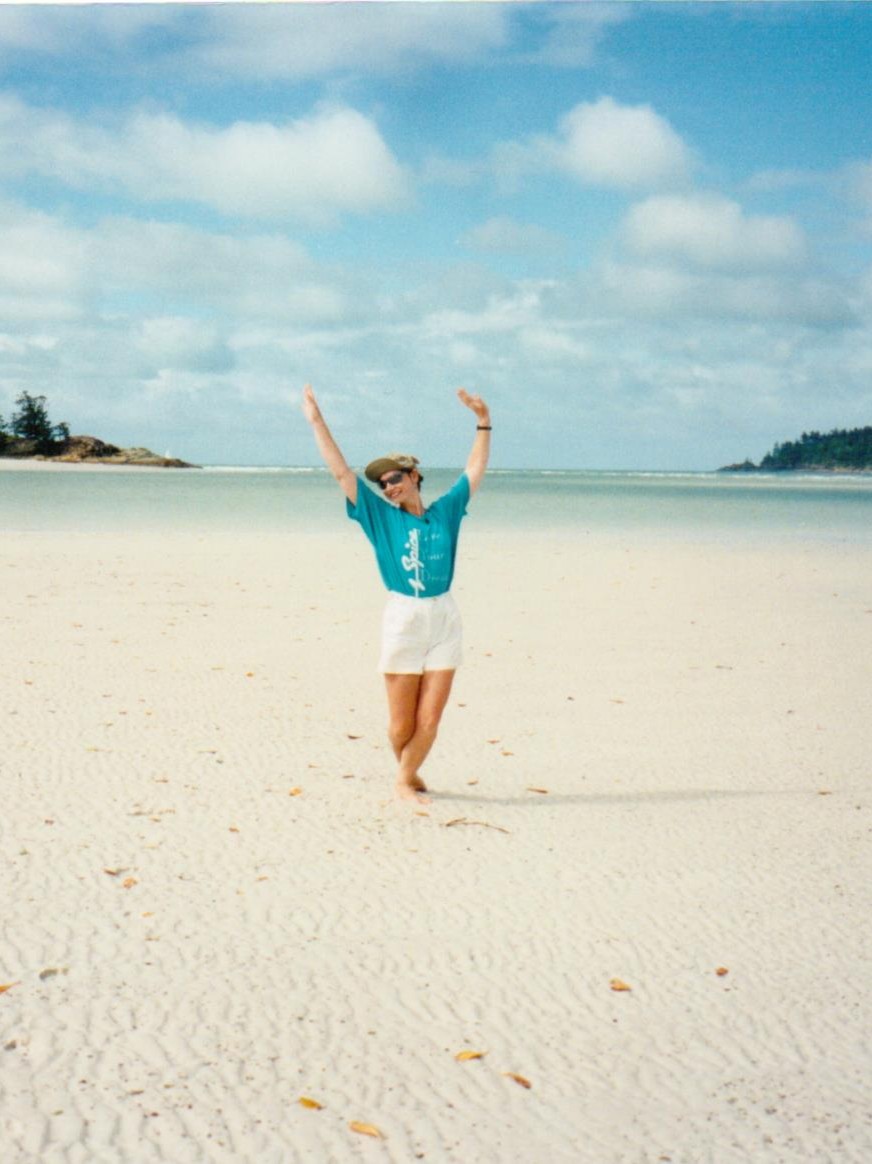 Author jacqueline lambert holding her arms aloft on the deserted white sand of Whitehaven Beach Australia