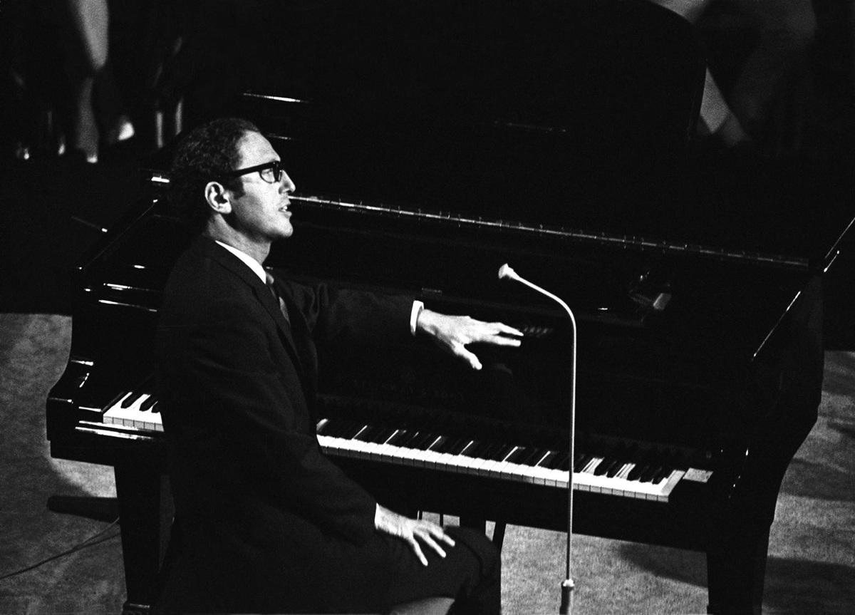 A black and white shot of Tom Lehrer with a piano as he performed in Copenhagen in 1967