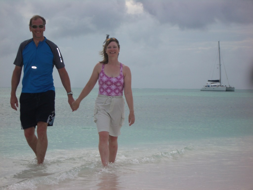 Author Jacqueline Lambert with husband Mark paddling in shallow sea with catamaran in the background British Virgin Islands