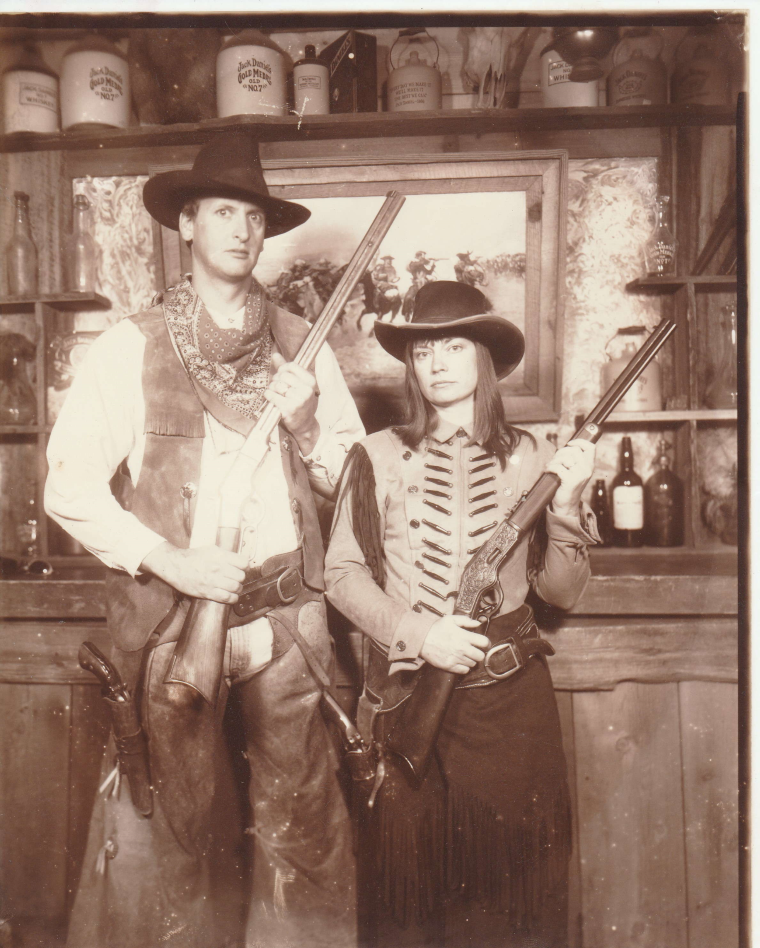 Author Jacqueline Lambert with husband Mark dressed as rifle-toting outlaws in a retro sepia tone photo 